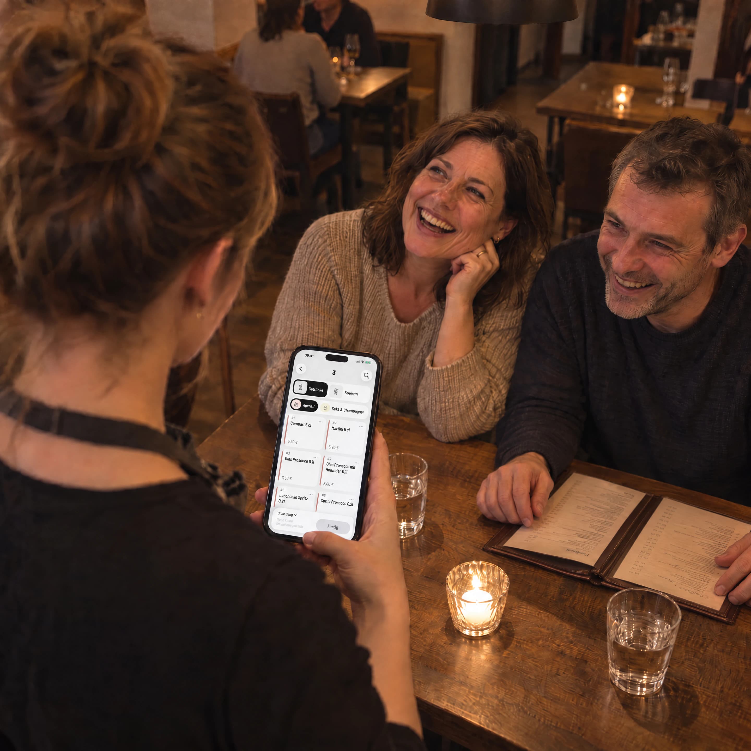 Servicekraft nimmt mit der Servire-App auf dem iPhone die Getränkebestellung eines Paares auf, beide lachen