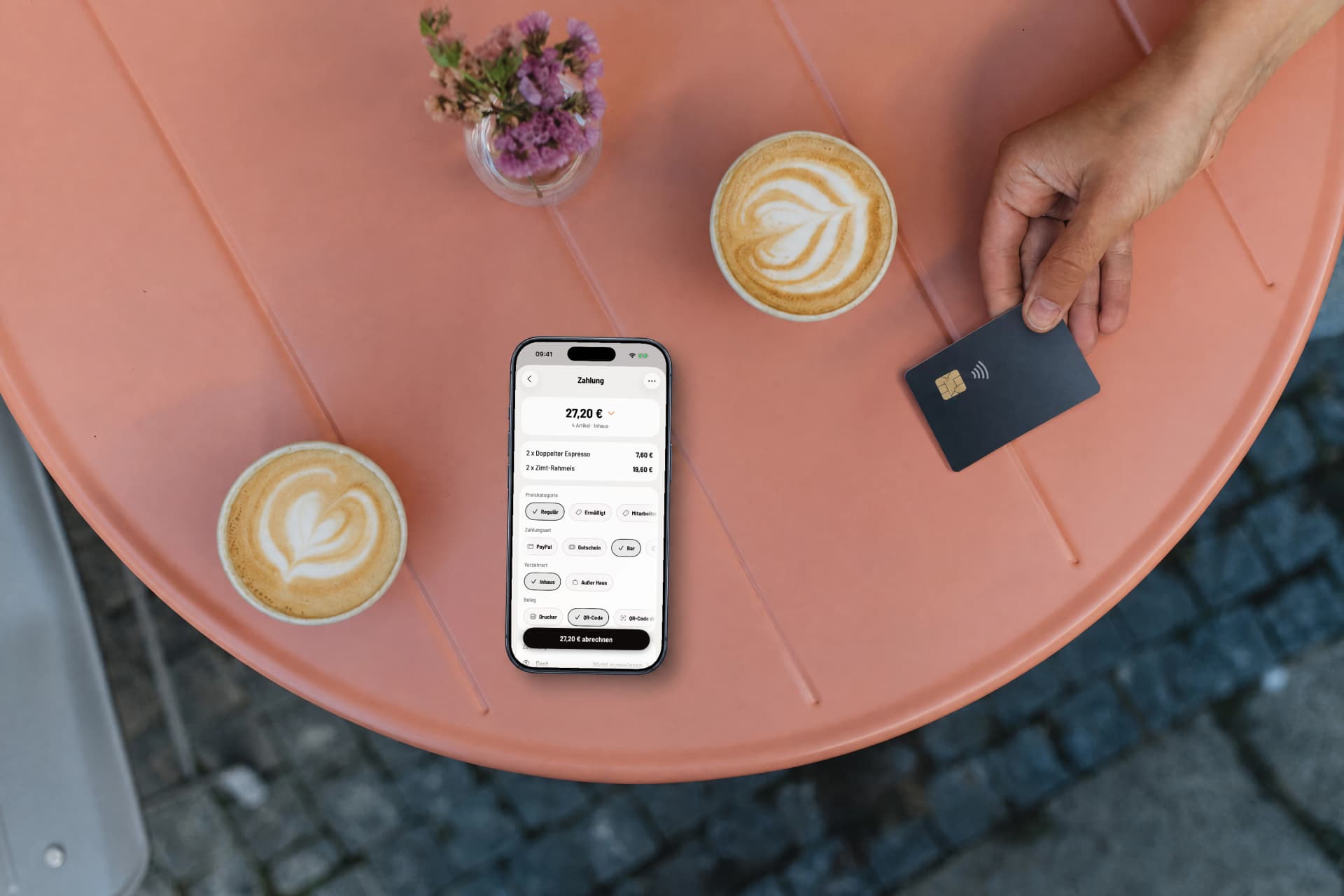Zahlungsbildschirm der Servire Kassen-App auf einem iPhone am Café-Tisch, daneben legt ein Gast eine Bankkarte ab