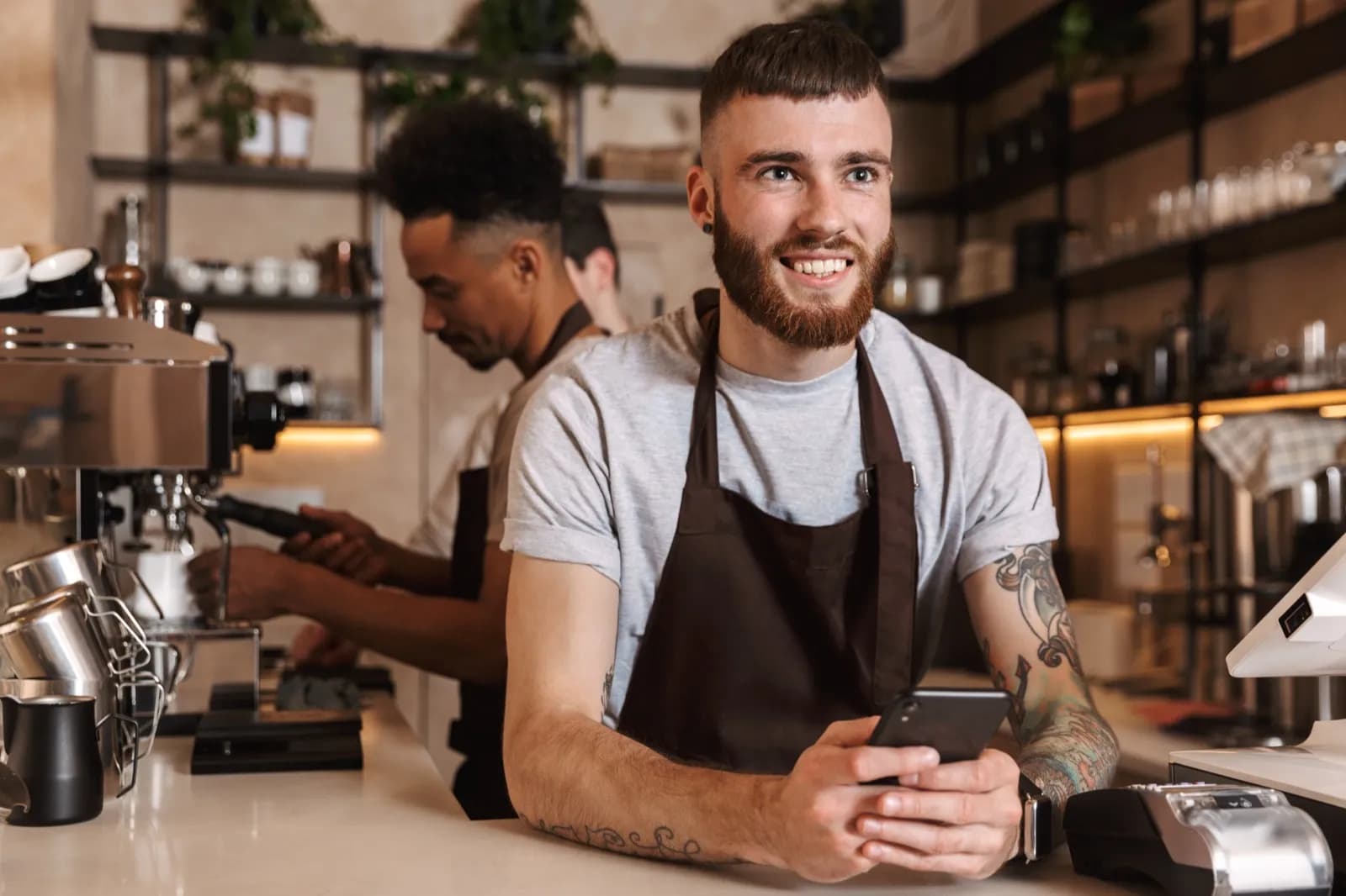 Barista mit Smartphone und Kollege an Kaffeemaschine